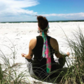 Woman sitting on beach with back to the camera. Hands on her knees in a meditative position